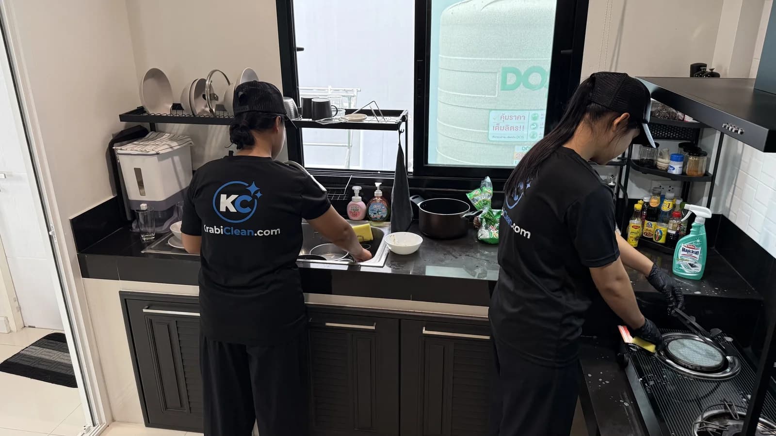 Two Krabi Clean cleaners in KrabiClean.com shirts, one washing up at the sink and one cleaning the hob