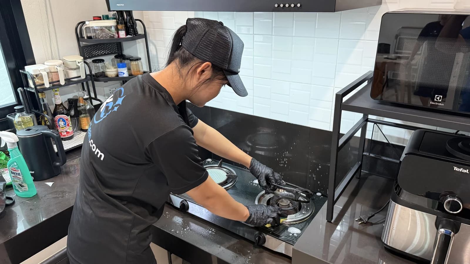 Krabi Clean cleaner in gloves scrubbing a glass gas hob with foam around the burners