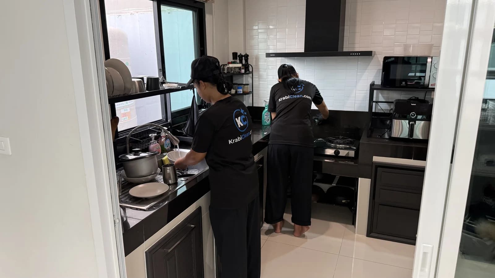 View from the kitchen door of two Krabi Clean cleaners working at the sink and the hob